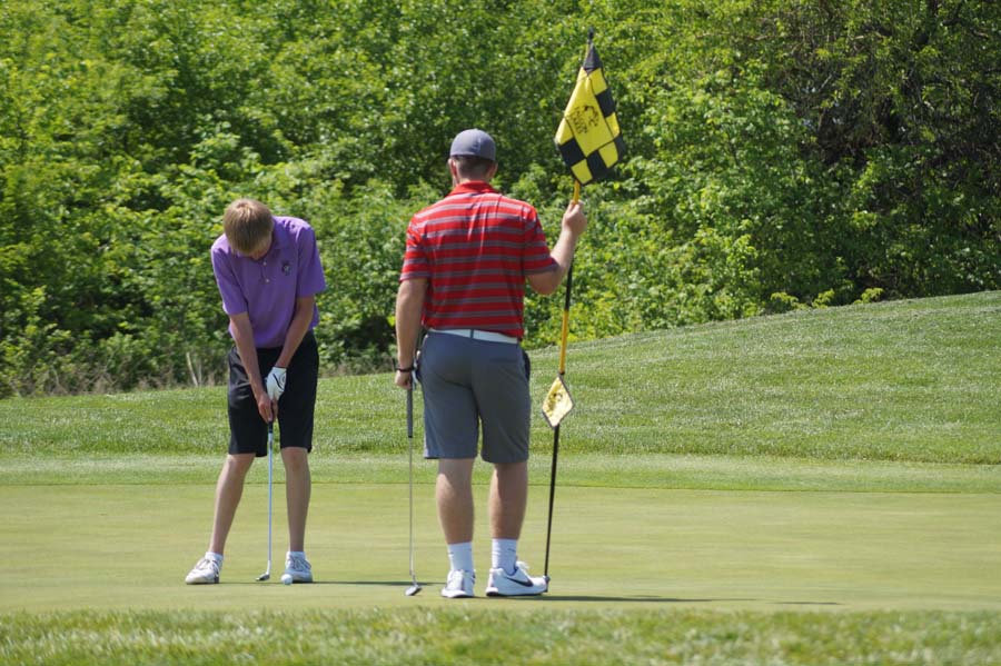 Junior Brian Hedlund makes the final shot while the other golfer holds the flag for him.