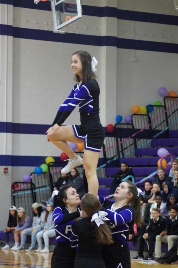 Sophomore Natalie Frick stunts at the court-warming pep rally with junior Emma Vogel and sophomore Allison Neal.