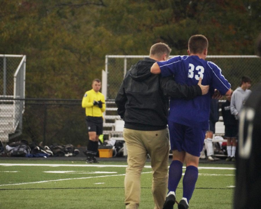 Freshman Evan Toms is helped off of the field by athletic trainer Troy Koerner. Toms was injured in a JV soccer game against Topeka-Hayden on Oct. 21 at Piper High School.