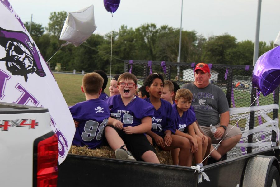While laughing and holding balloons, elementary football players ride on their float.